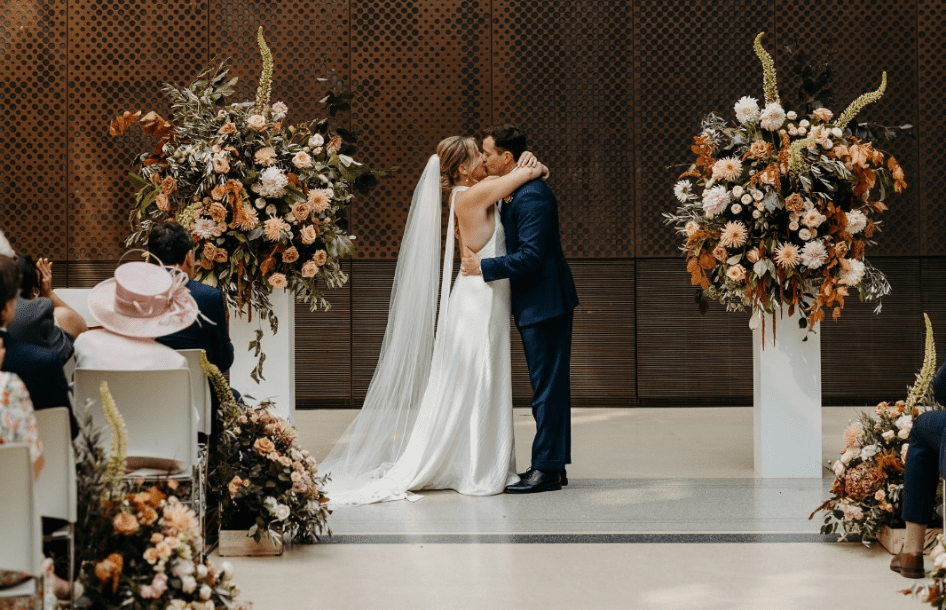 A couple kiss surrounded by huge floral displays